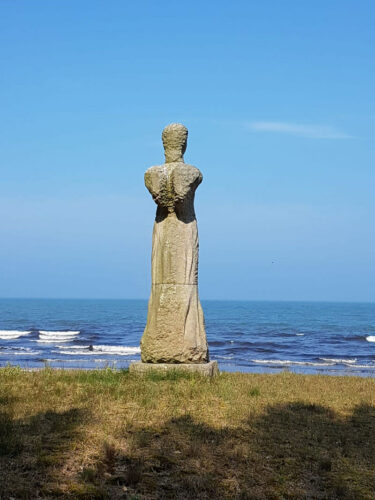Ein Engeldenkmal aus Stein, dahinter das Meer.