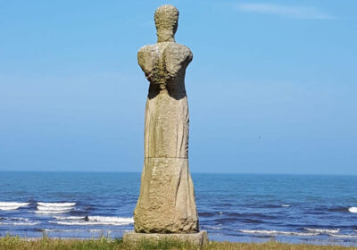 Ein Engeldenkmal aus Stein, dahinter das Meer.