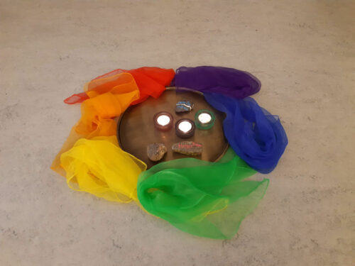 Gestaltete Mitte mit Teelichtern und außen rum bunte Tücher in Regenbogenfarben.