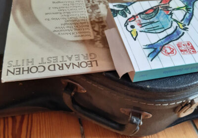 Leonard Cohen Schallplatte und Buch liegen auf einem Gitarrenkoffer.