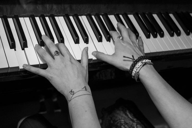 Klaviertasten, auf denen jemand mit den Händen spielt. Die Hände tragen Ringe und Armbänder.